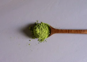 Cuillère en bois avec du matcha sur fond gris.